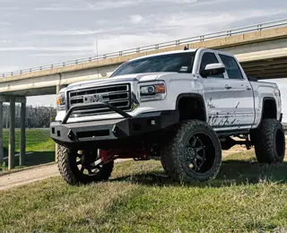 A lifted pickup truck sits atop a hill framed by a nearby roadway