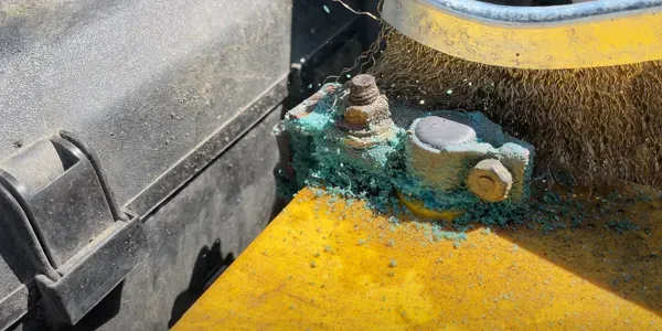 Cleaning corrosion from a battery terminal with a wire brush.