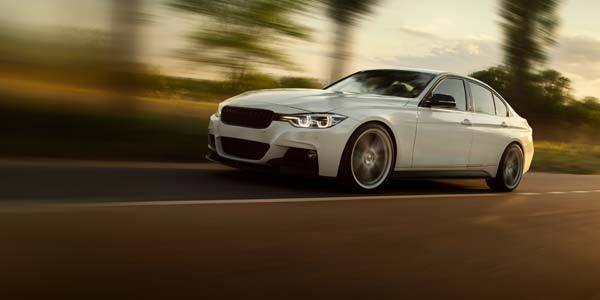 White BMW style car speeding down road.