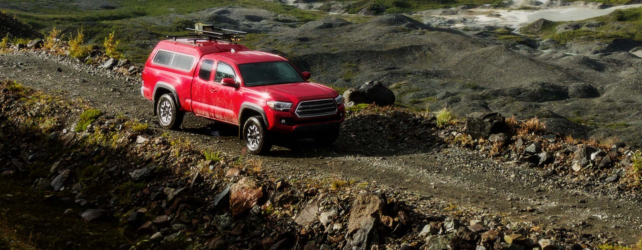Red pickup with canopy on rough rock road.
