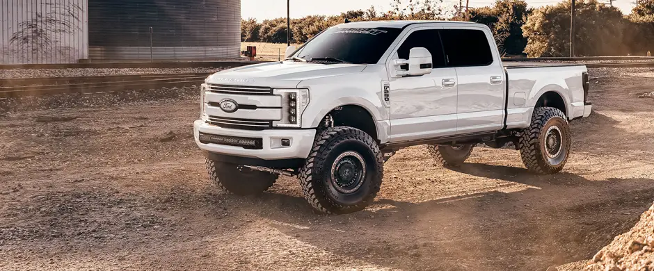 Large lifted white truck in a gravel lot.