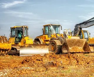 A row of construction equipment lined up in a dirt-filled construction site.