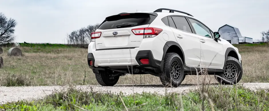 Small silver truck with camper driving over rough gravel road.